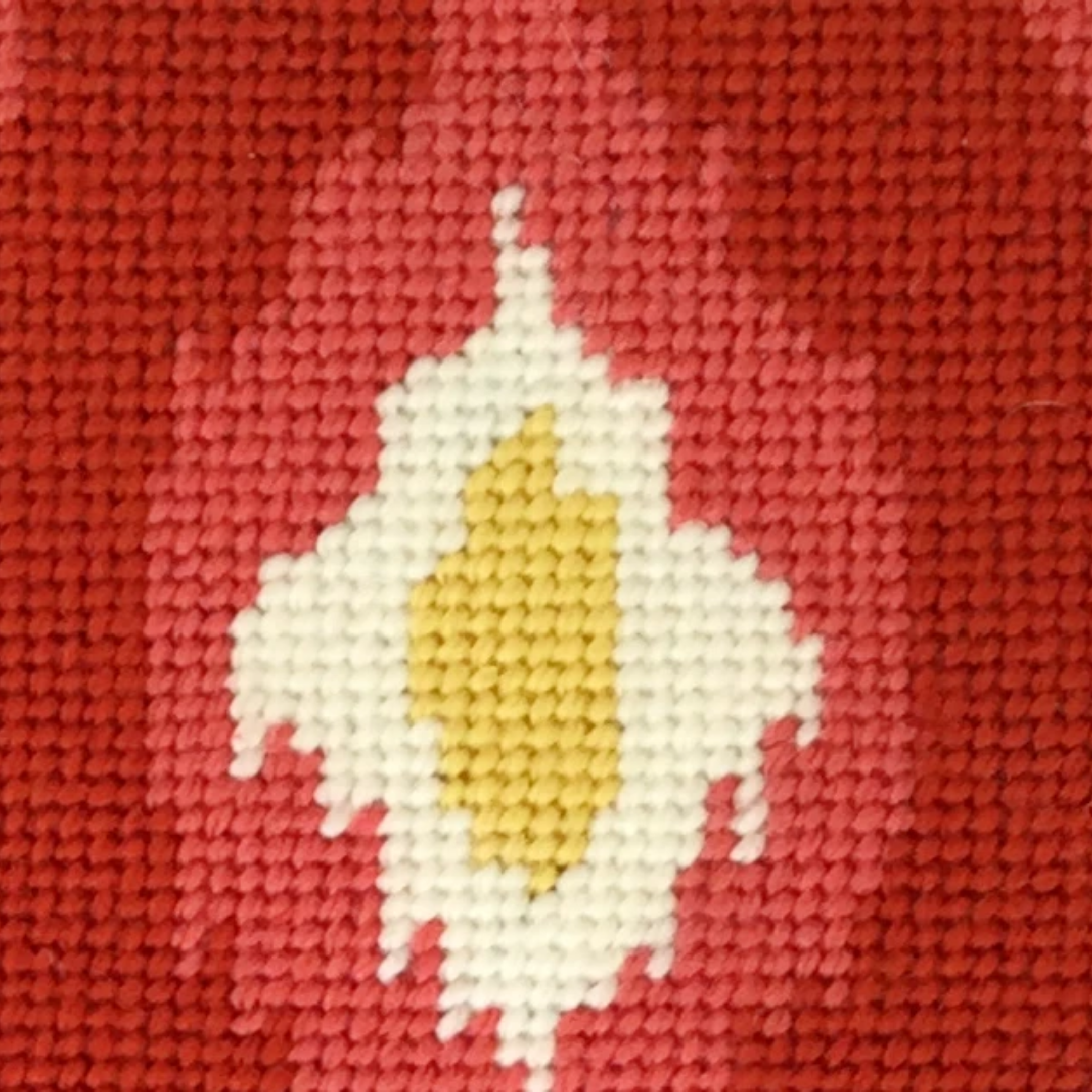 Cross-stitched design of a sun on red fabric