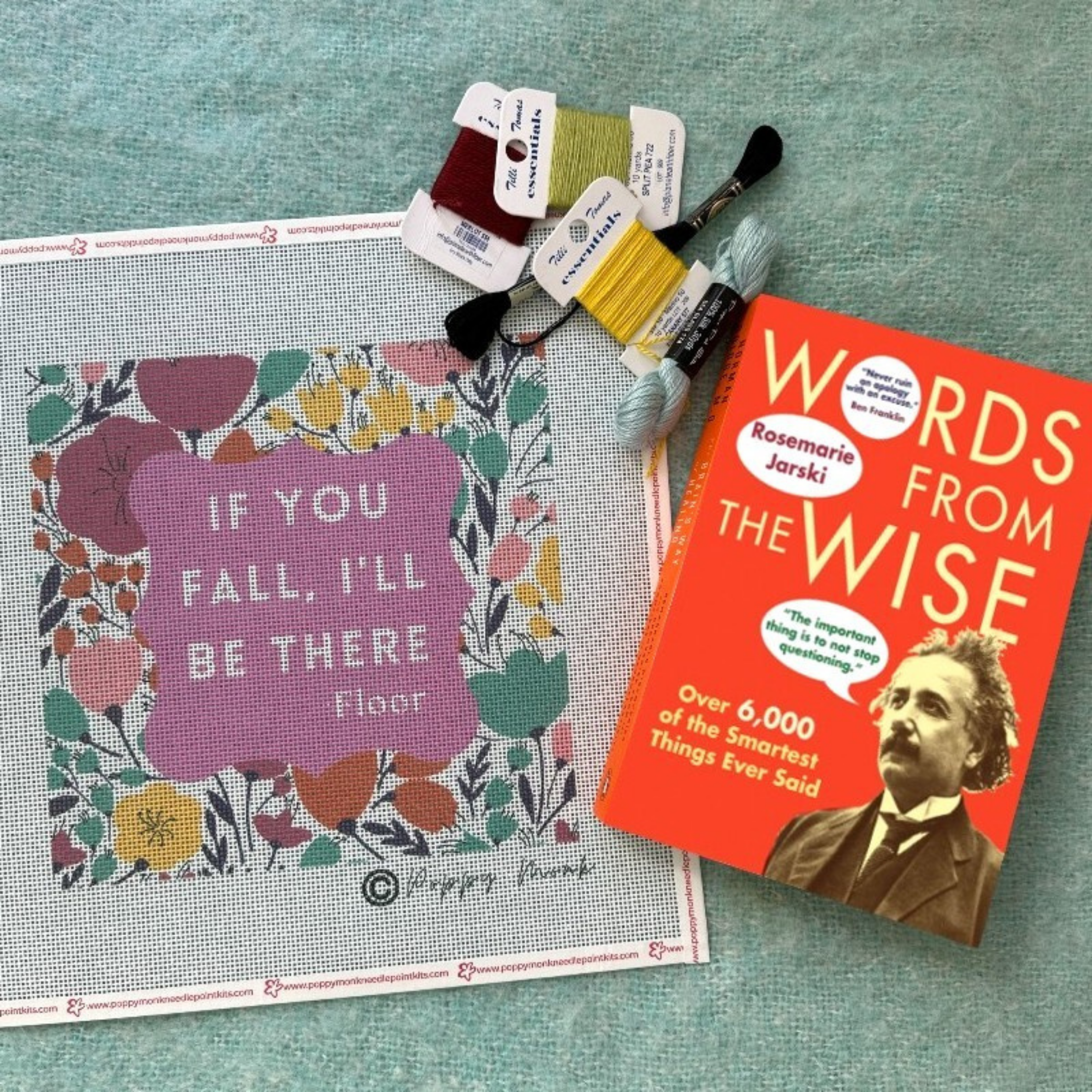 Cross-stitch pattern with floral design and motivational quote, next to a book titled 'Words from the Wise' on a textured surface.