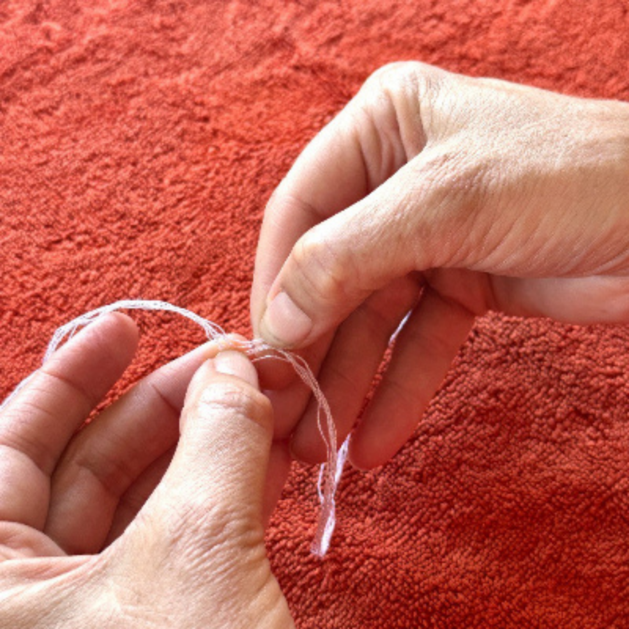 Close-up of hands holding a piece of string against a red textured background