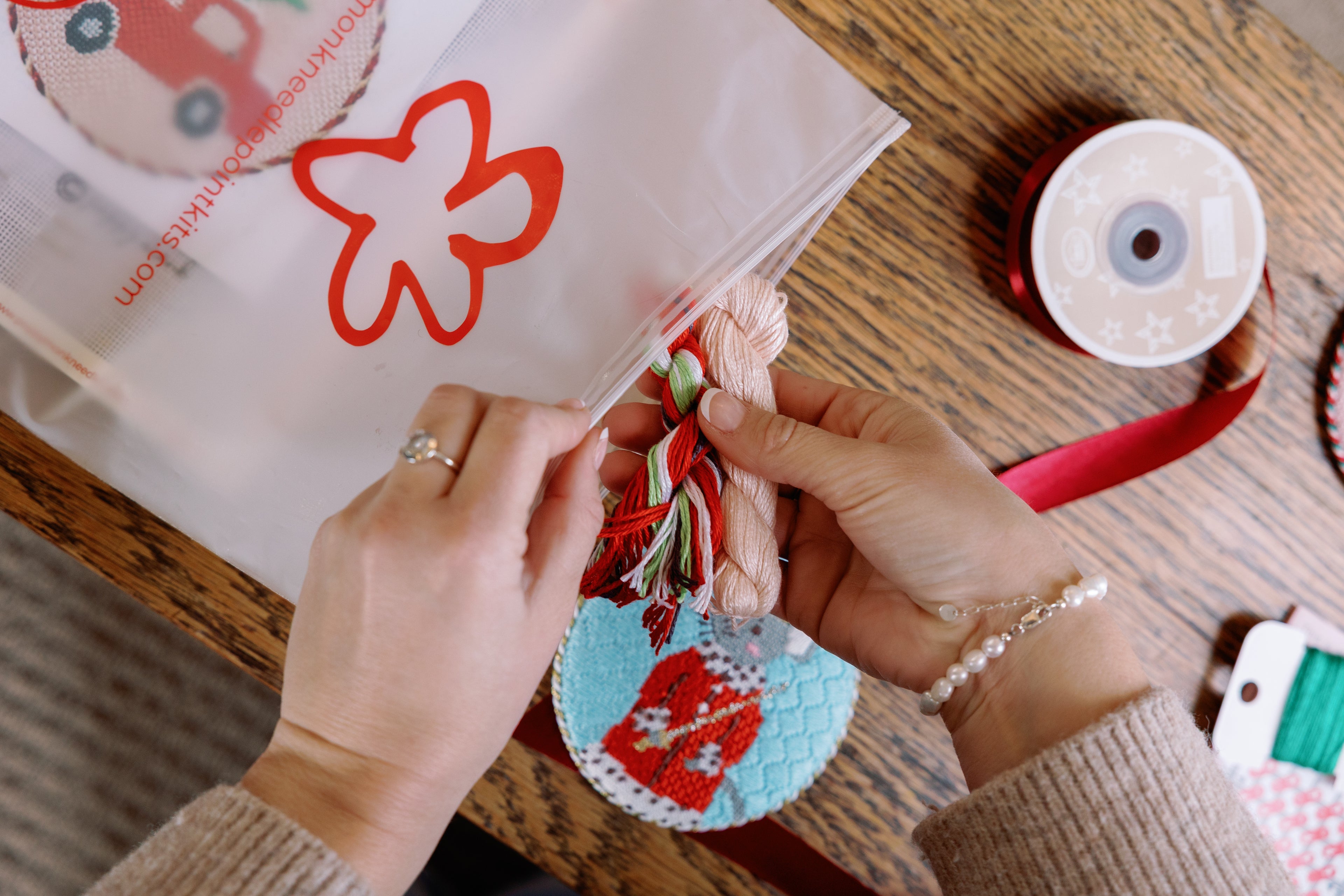Person decorating a gift with red and blue designs on a wooden table.