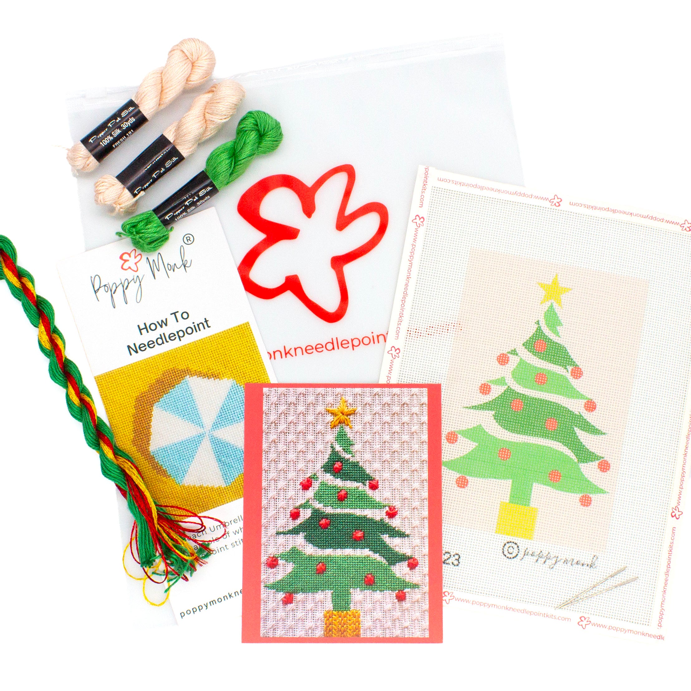 A flat lay image of everything that comes in the Christmas Tree kit. This includes a canvases with the printed Christmas Tree design, a card with a photo of the finished stitched design, an instructional brochure, and threads on top of a Poppy Monk bag with the poppy logo on it.