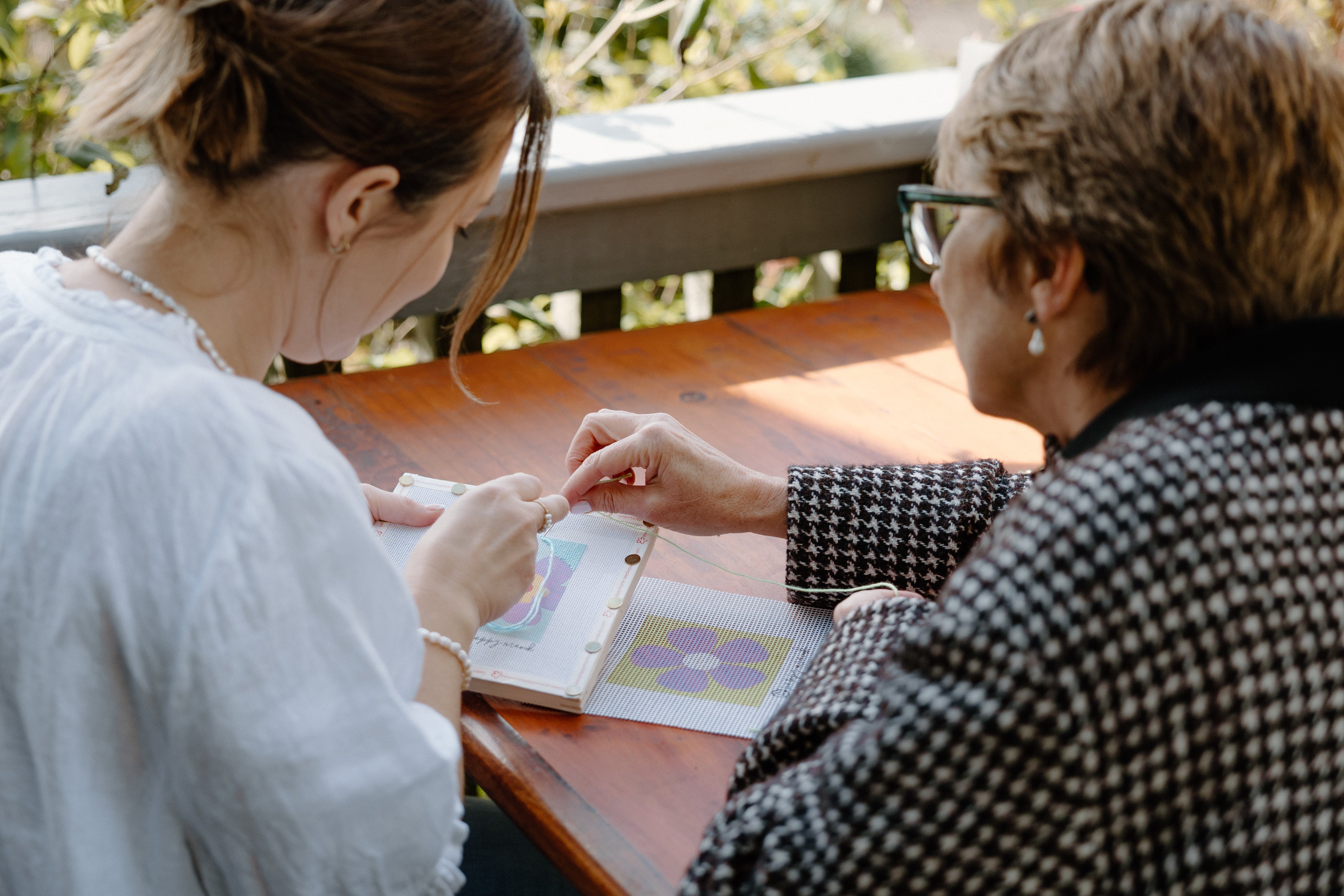 Two women sitting at a table outdoors, one showing a book to the other.