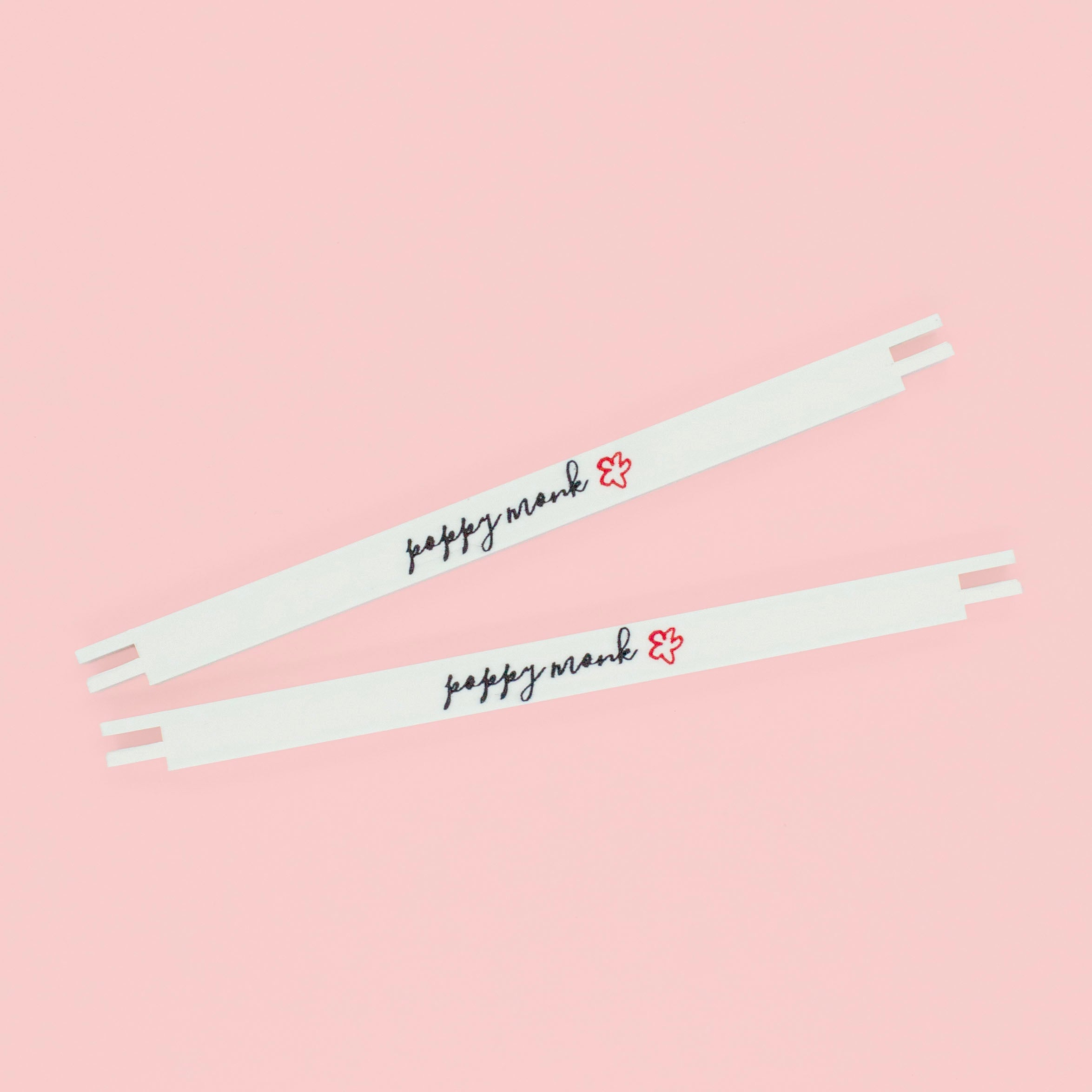 Two white stretcher bars with the Poppy Monk logo printed on them lying on a pink background.