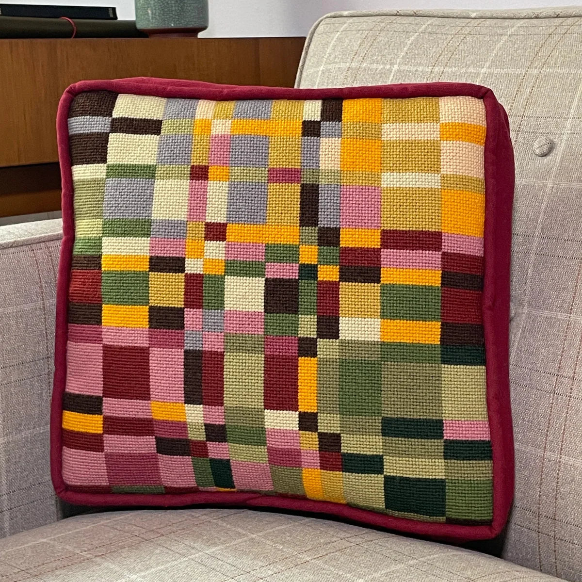 A square needlepoint pillow of geometric design resting on a chair