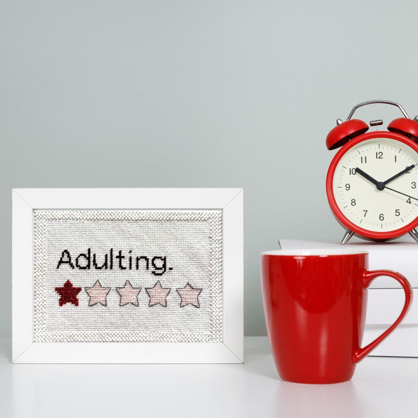 Adulting needlepoint in a frame on a desk