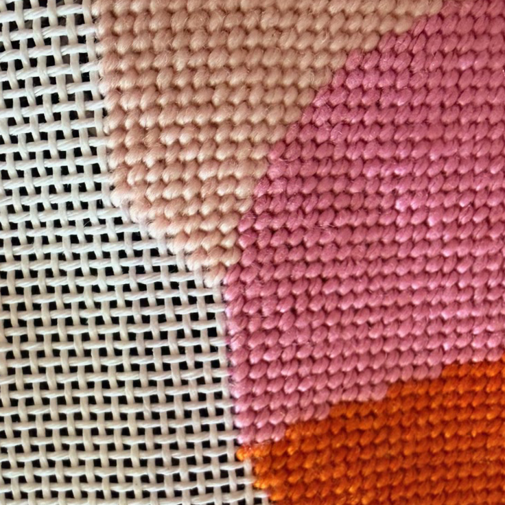 Close-up of a needlepoint fabric with pink and orange patterns on a pink background.