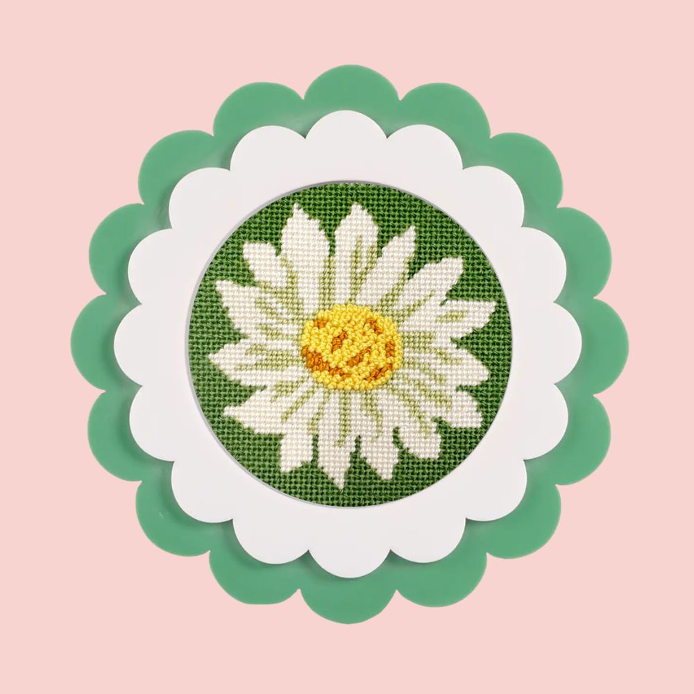 A daisy needlepoint round with decorative stitches shown in a green scalloped frame