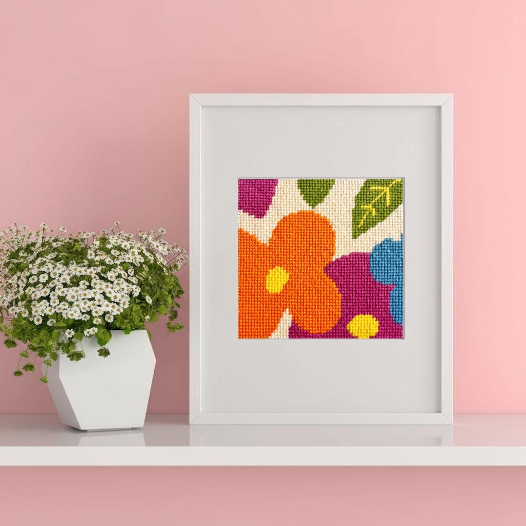 Framed needlepoint floral artwork on a pink wall with a potted plant.