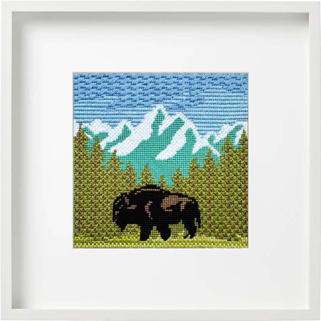 Framed cross-stitched artwork of a mountain landscape with a bison.