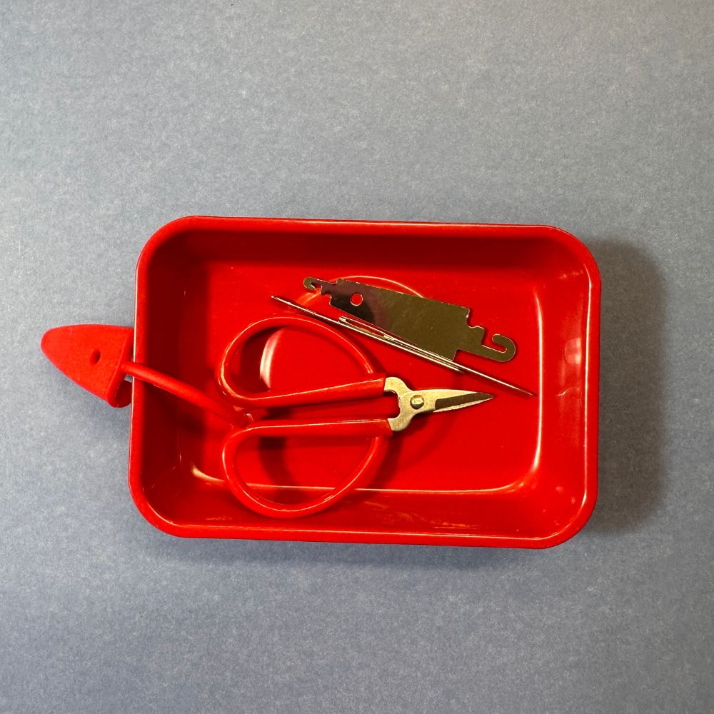 Red metal tray with scissors and a bottle opener on a gray background