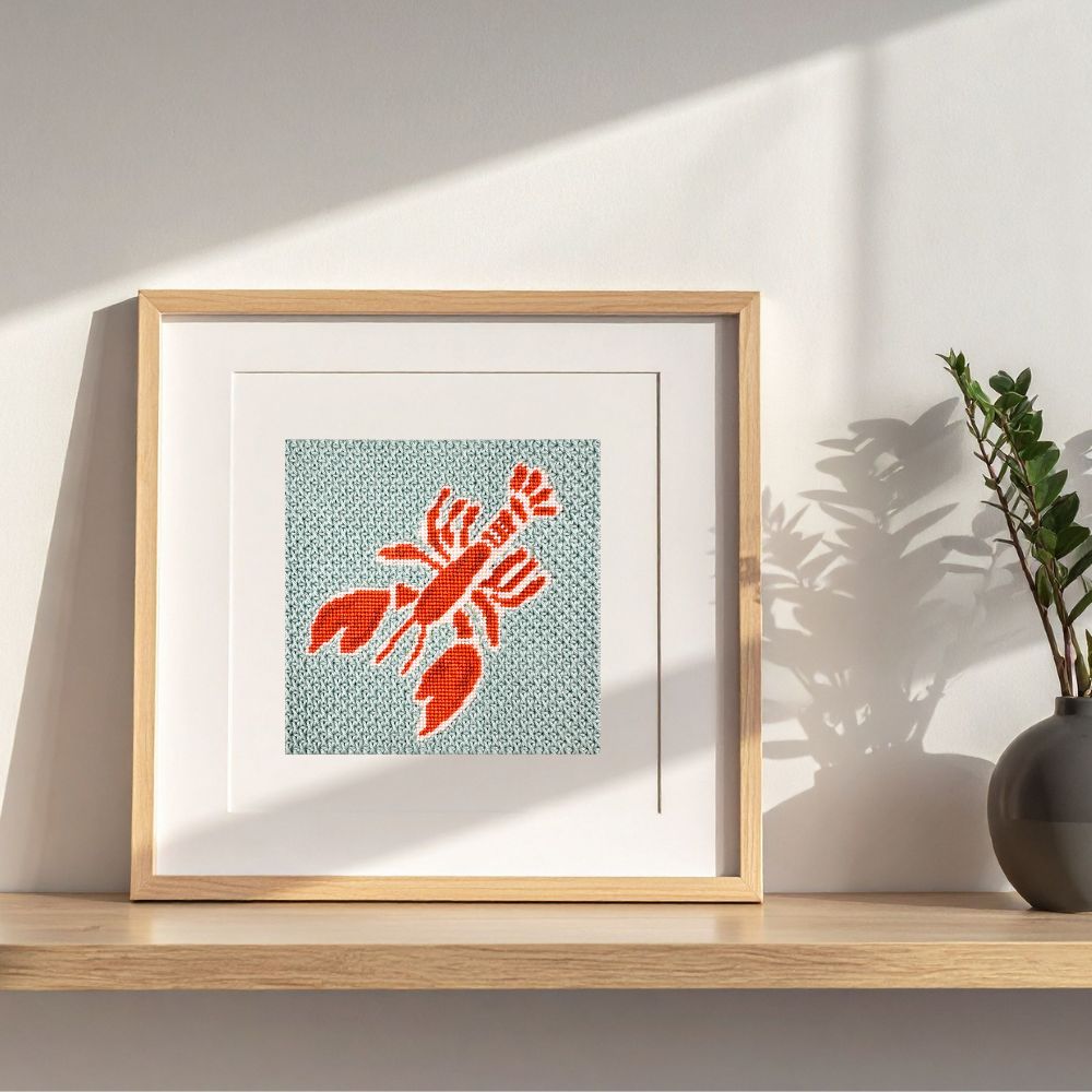 Lobster needlepoint design shown in a frame on a shelf