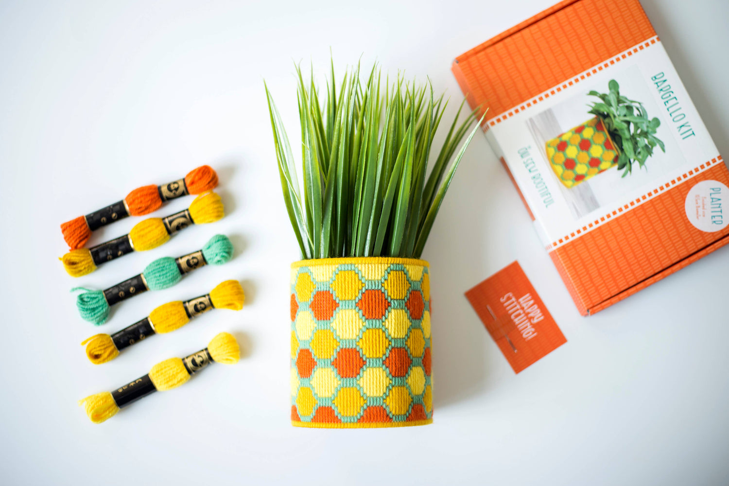 Decorative plant pot with colorful hexagonal pattern, grass, and craft materials on a white background