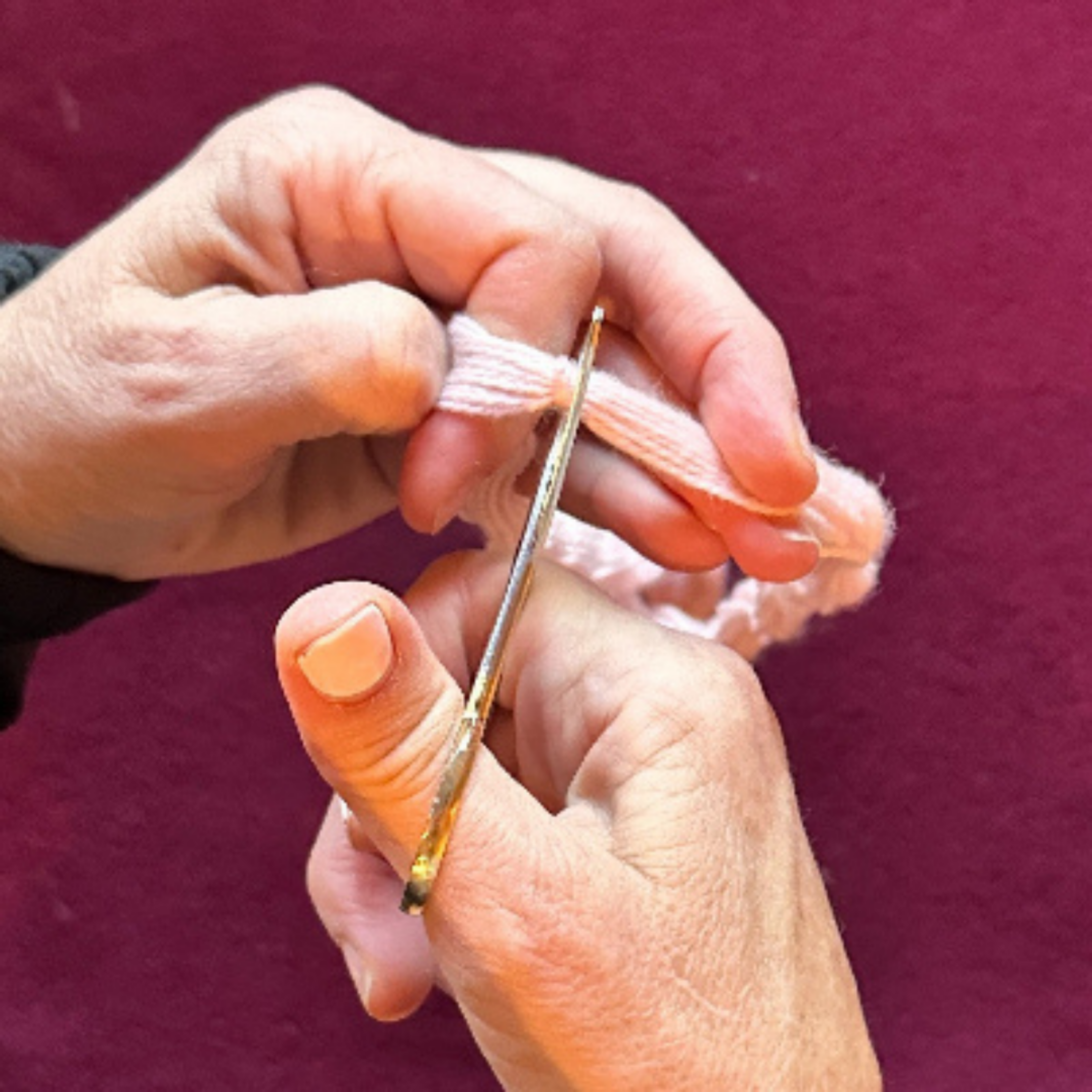 Close-up of hands using a needle and pink thread against a purple background