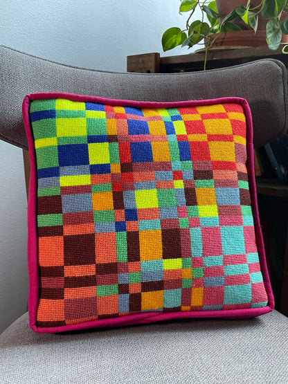 Colorful checkered pillow on a gray couch with a plant in the corner.