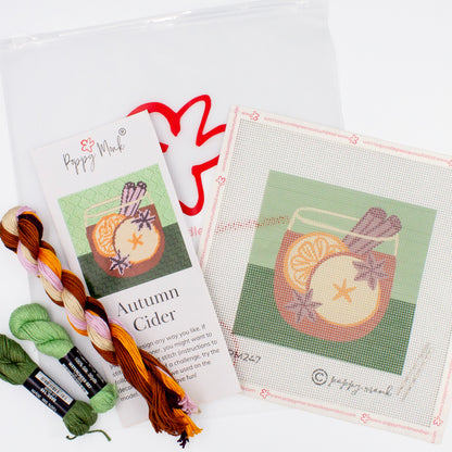 The Autumn Cider Kit components on a white backdrop. This includes the canvas with the printed design, colorful threads, instructional brochure, and a bag with the Poppy Monk logo on it.