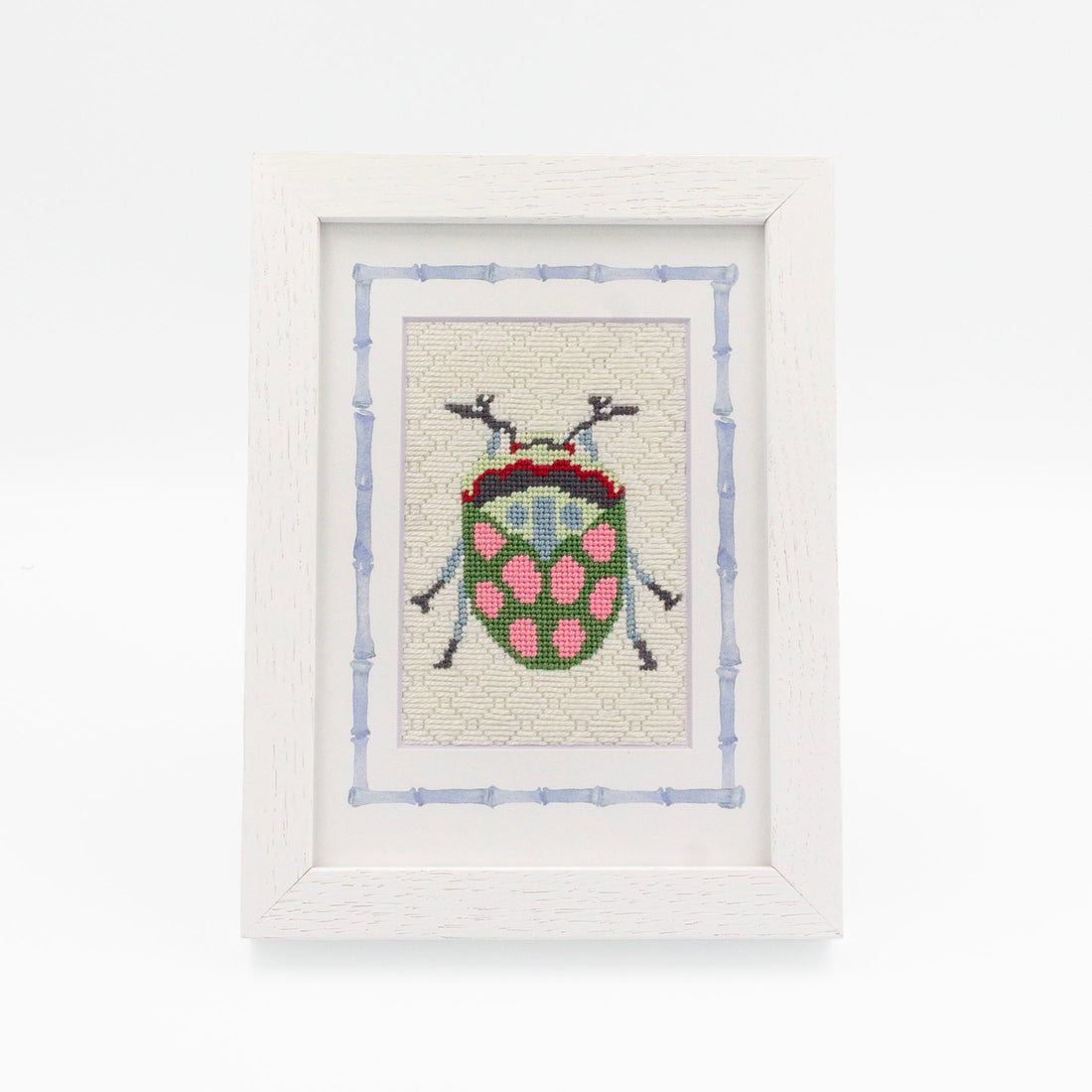 The Beetle kit stitched and in a white frame with a mat with a decorative blue watercolor bamboo border.