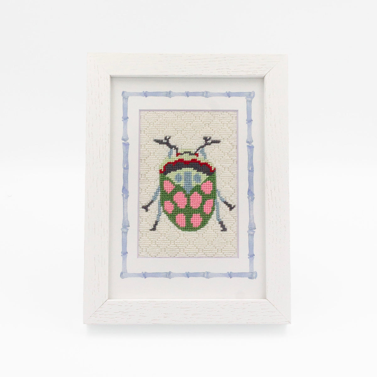 The Beetle kit stitched and in a white frame with a mat with a decorative blue watercolor bamboo border.