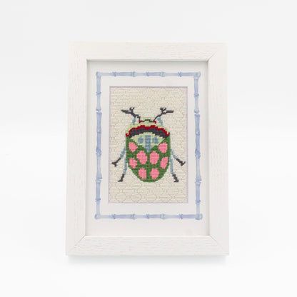 The Beetle kit stitched and in a white frame with a mat with a decorative blue watercolor bamboo border.