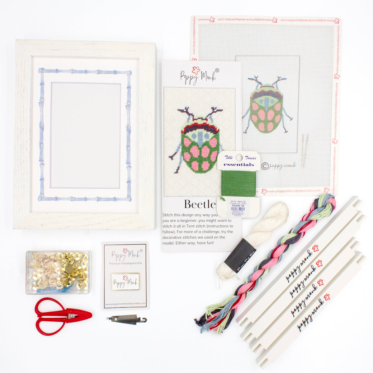 The Beetle kit components on a white background. There is a white frame with a mat with a decorative blue watercolor bamboo border, the canvas with the design, an instructional brochure, colorful threads, tacks, red scissors, a Poppy Monk needle minder, a needle threader, and four Poppy Monk stretcher bars.