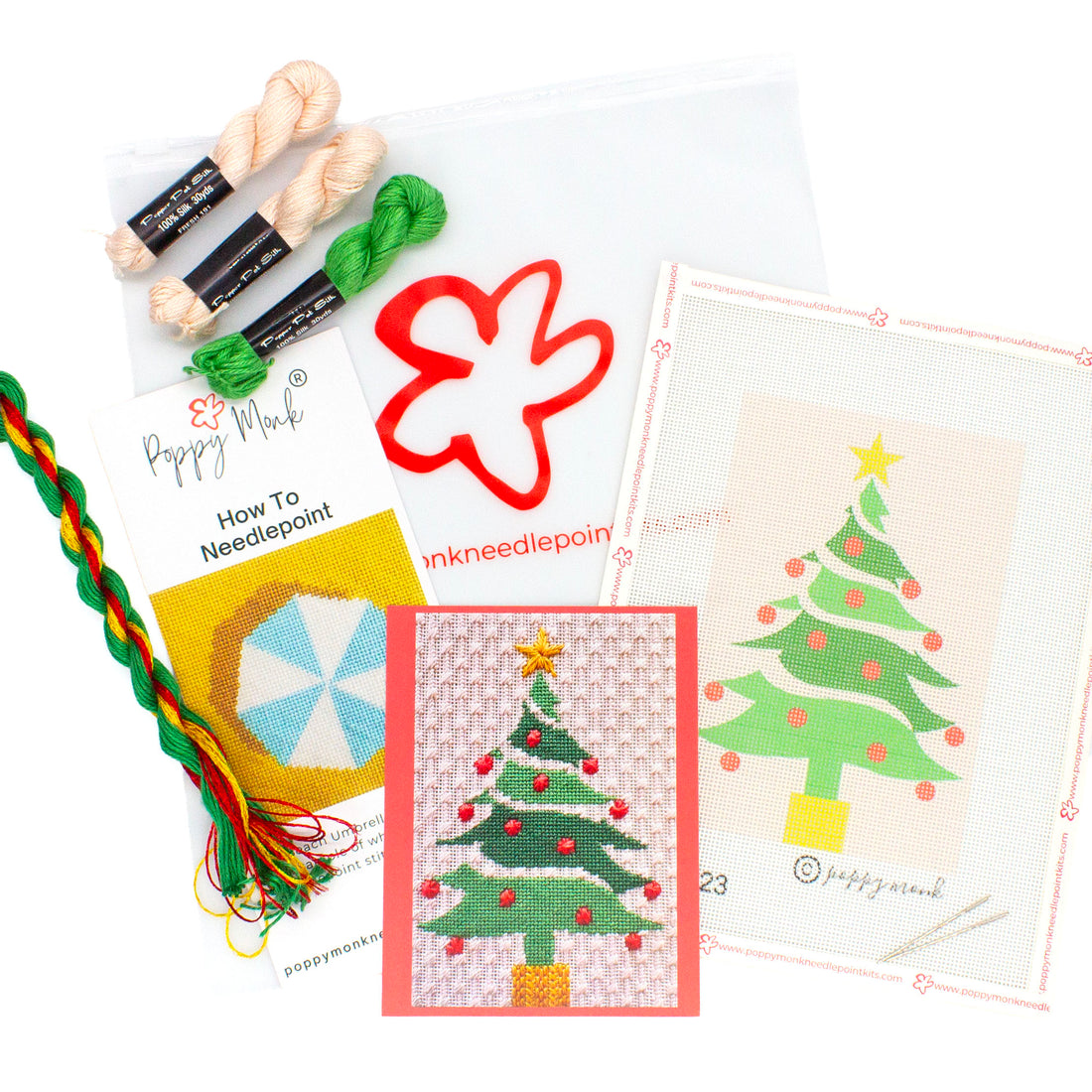 A flat lay image of everything that comes in the Christmas Tree kit. This includes a canvases with the printed Christmas Tree design, a card with a photo of the finished stitched design, an instructional brochure, and threads on top of a Poppy Monk bag with the poppy logo on it.