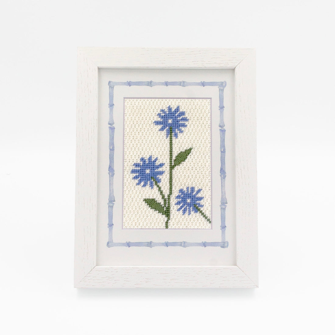 The Cornflower kit stitched and in a white frame with a mat with a decorative blue watercolor bamboo border.