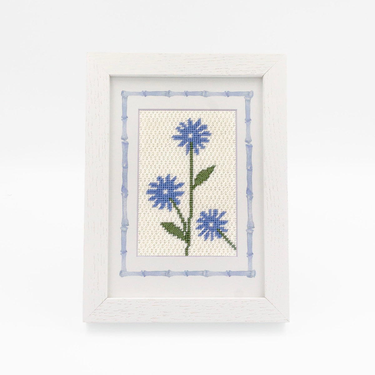 The Cornflower kit stitched and in a white frame with a mat with a decorative blue watercolor bamboo border.