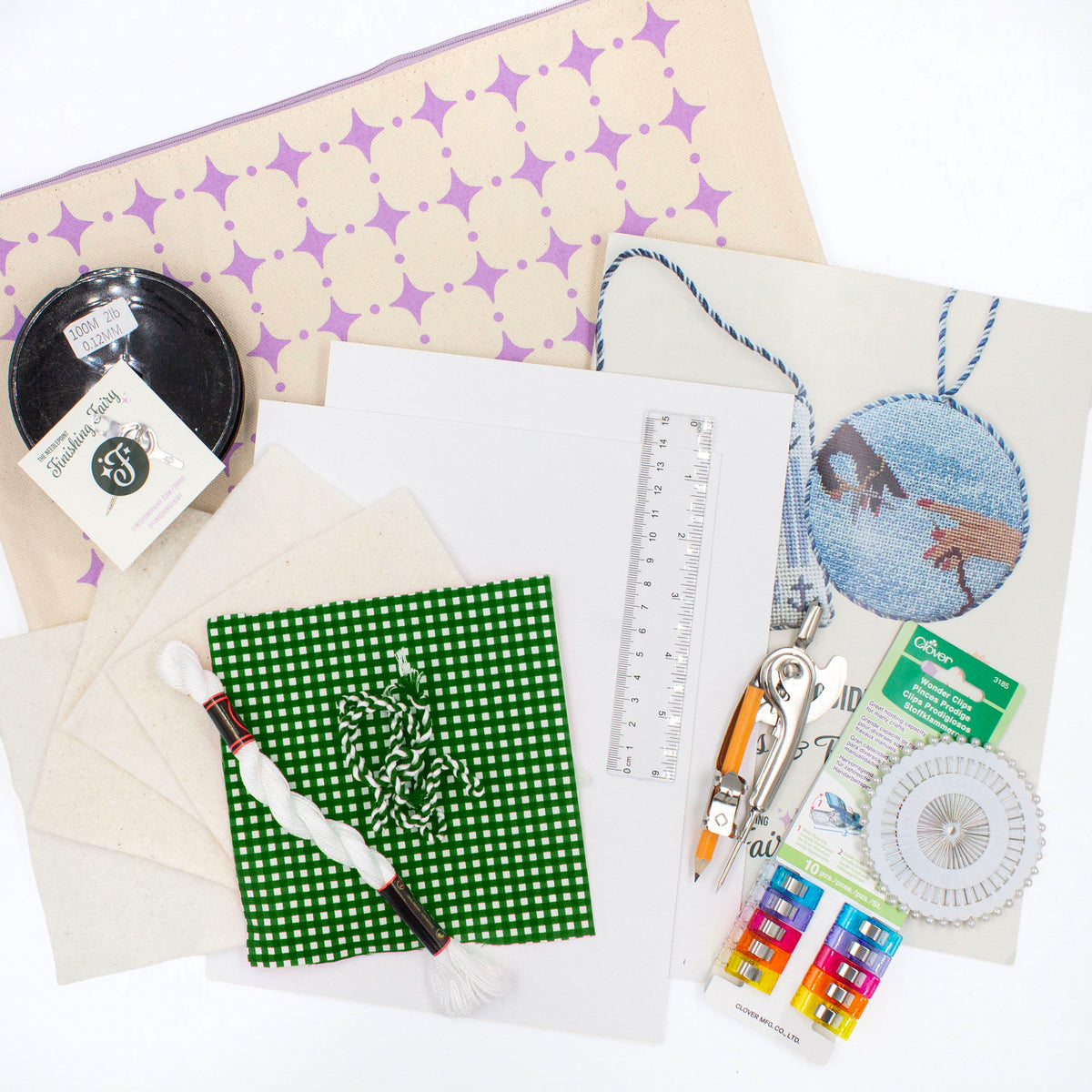 The Finishing Kit components on a white background. This includes green and white gingham fabric and matching cording, four squares of batting, white thread, cardstock, a ruler, a compass, sewing clips and pins, fishing line, needle, needle threader, instruction booklet, and canvas carry bag.