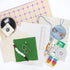 The Finishing Kit components on a white background. This includes green and white gingham fabric and matching cording, four squares of batting, white thread, cardstock, a ruler, a compass, sewing clips and pins, fishing line, needle, needle threader, instruction booklet, and canvas carry bag.
