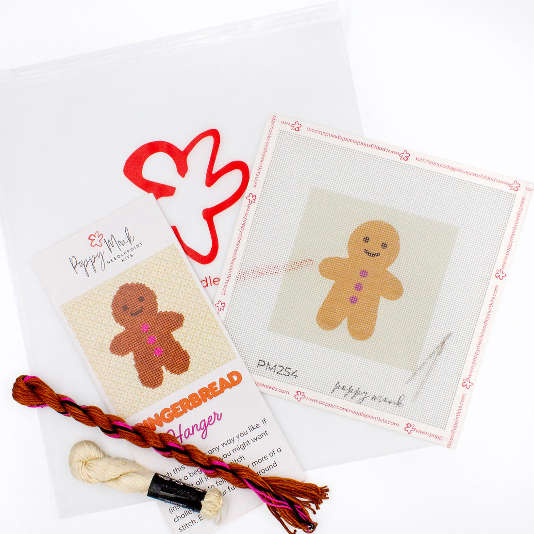 The Gingerbread kit components on a white background. There is a canvas with the design, an instructional brochure, colorful threads, needles, and clear bag with the Poppy Monk logo on it.