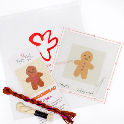The Gingerbread kit components on a white background. There is a canvas with the design, an instructional brochure, colorful threads, needles, and clear bag with the Poppy Monk logo on it.