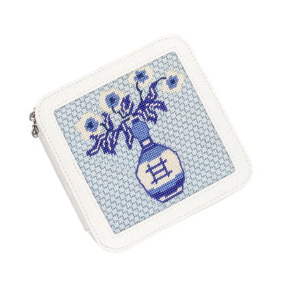 A white faux-leather zippered coin purse featuring a blue and white cross-stitch style illustration of a vase with flowers on the front.