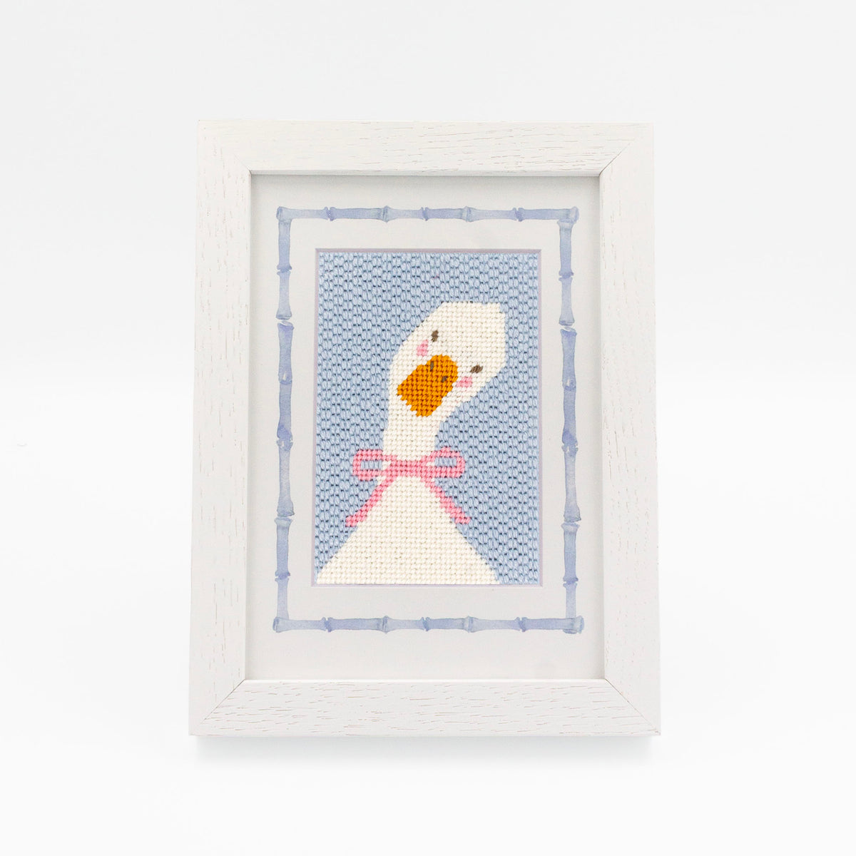 The Lucy Goosey kit stitched and in a white frame with a mat with a decorative blue watercolor bamboo border.