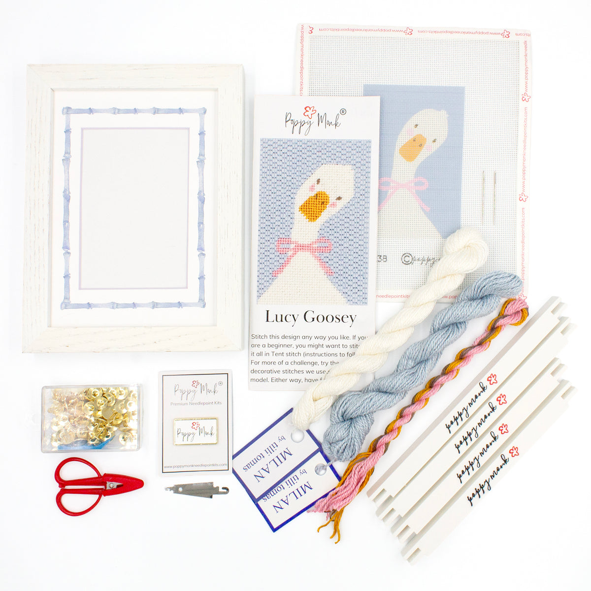 The Lucy Goosey kit components on a white background. There is a white frame with a mat with a decorative blue watercolor bamboo border, the canvas with the design, an instructional brochure, colorful threads, tacks, red scissors, a Poppy Monk needle minder, a needle threader, and four Poppy Monk stretcher bars.