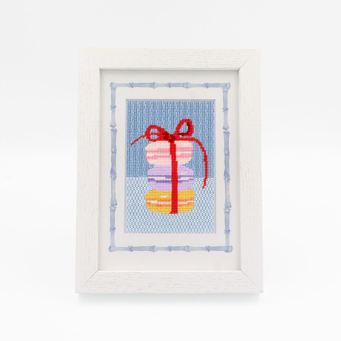 The Macaroons kit stitched and in a white frame with a mat with a decorative blue watercolor bamboo border.