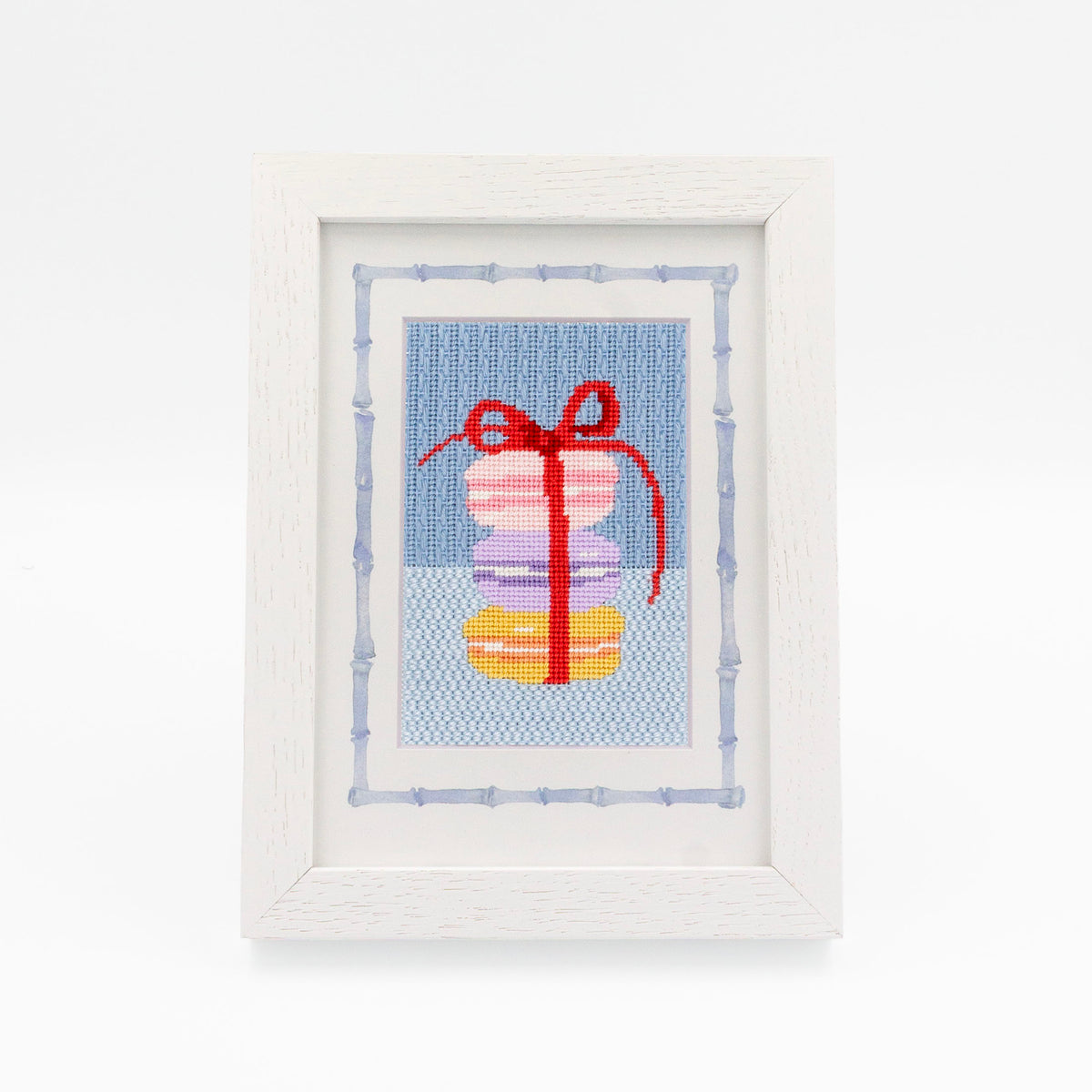 The Macaroons kit stitched and in a white frame with a mat with a decorative blue watercolor bamboo border.