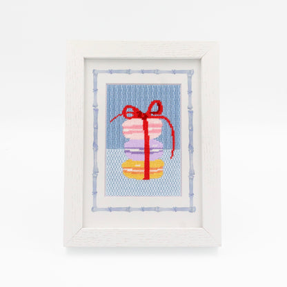 The Macaroons kit stitched and in a white frame with a mat with a decorative blue watercolor bamboo border.
