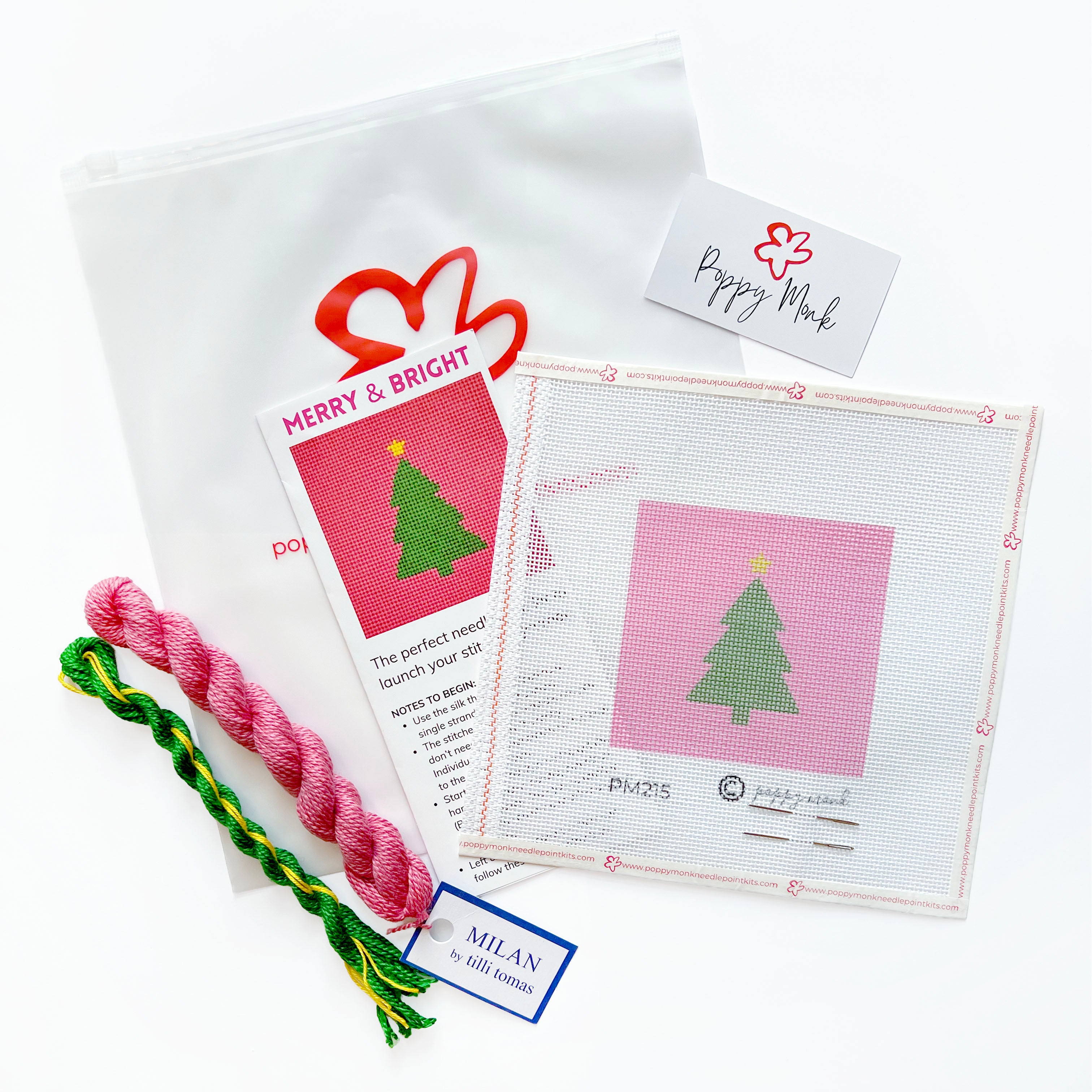 A Christmas-themed needlepoint kit featuring a white mesh canvas with a pink background and green tree design, a pink and green braided cord, a white drawstring pouch, and printed instruction cards on a white background.