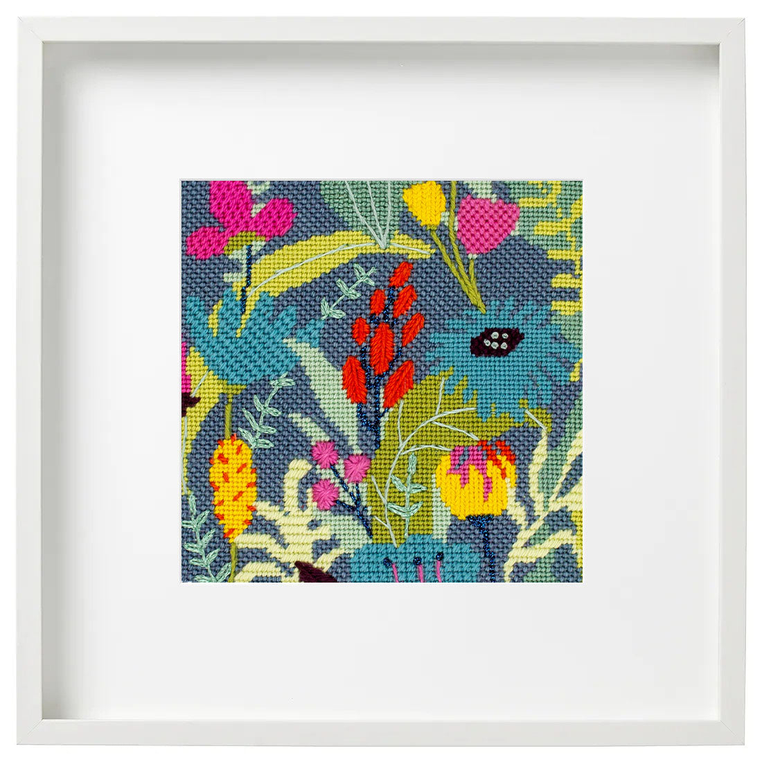 A framed square canvas print featuring a colorful floral and botanical pattern on a dark blue-gray background, set within a wide white frame.