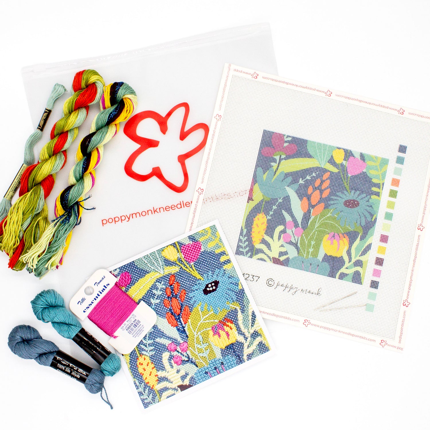 The kit components of Midnight Garden laying on a white background. There is a canvas with the printed design, colorful threads, an instruction card with a photo of the stitched piece, and a bag with the Poppy Monk logo.