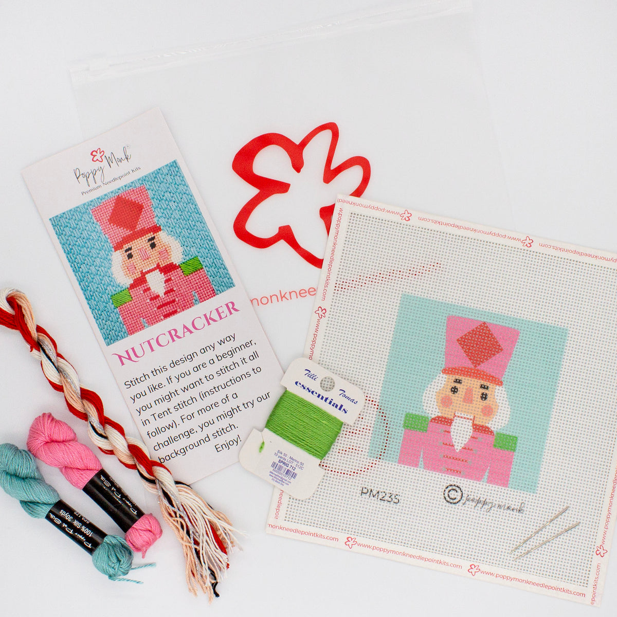 The kit components of the Festive Nutcracker laying on a white background. There is a canvas with the printed design, colorful threads, an instruction brochure with a photo of the stitched piece, and a bag with the Poppy Monk logo.