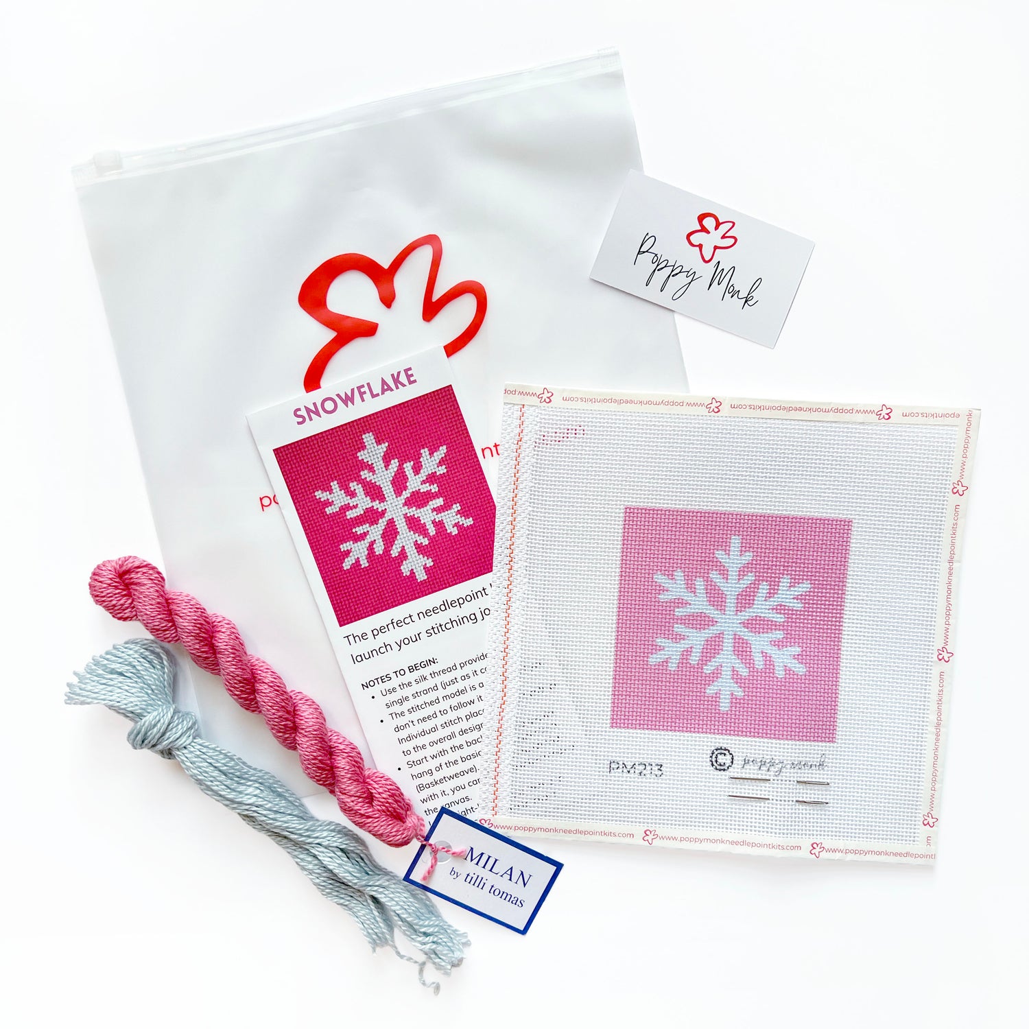 A craft kit laid out on a white background, including a white canvas bag with a red logo, a printed instruction card titled SNOWFLAKE, a pink-and-white swatch card, two skeins of thread in pink and light blue.