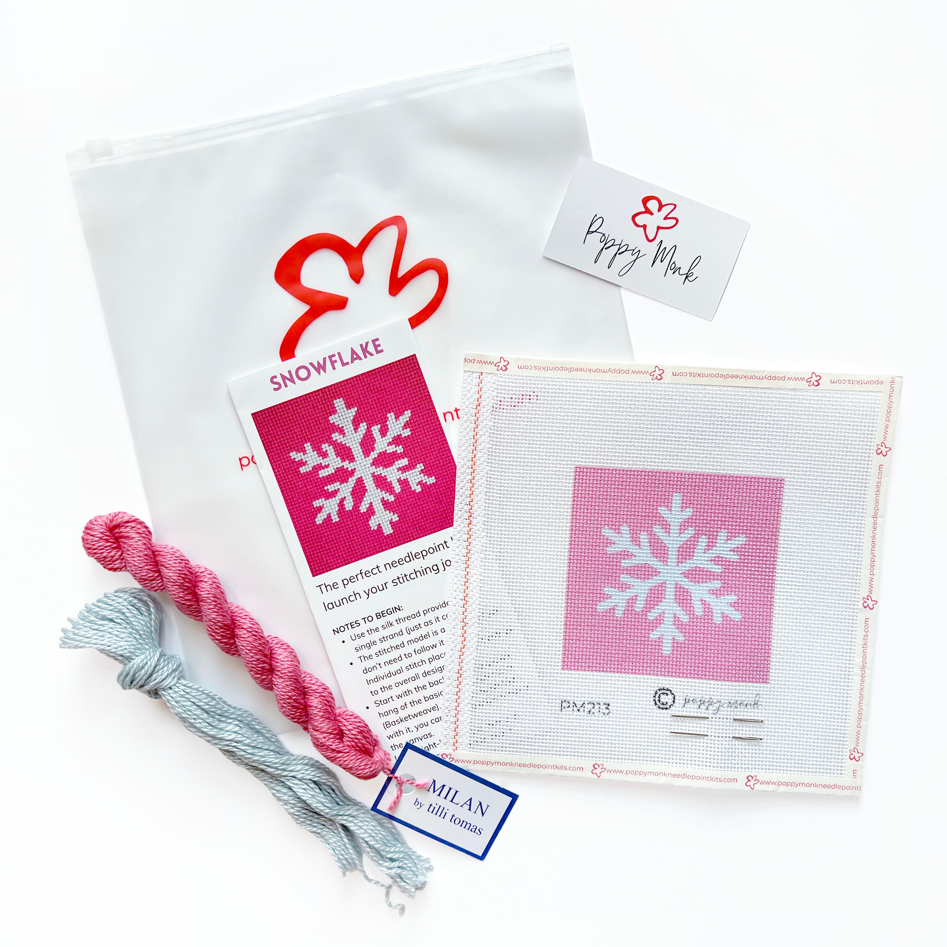 A craft kit laid out on a white background, including a white canvas bag with a red logo, a printed instruction card titled SNOWFLAKE, a pink-and-white swatch card, two skeins of thread in pink and light blue.