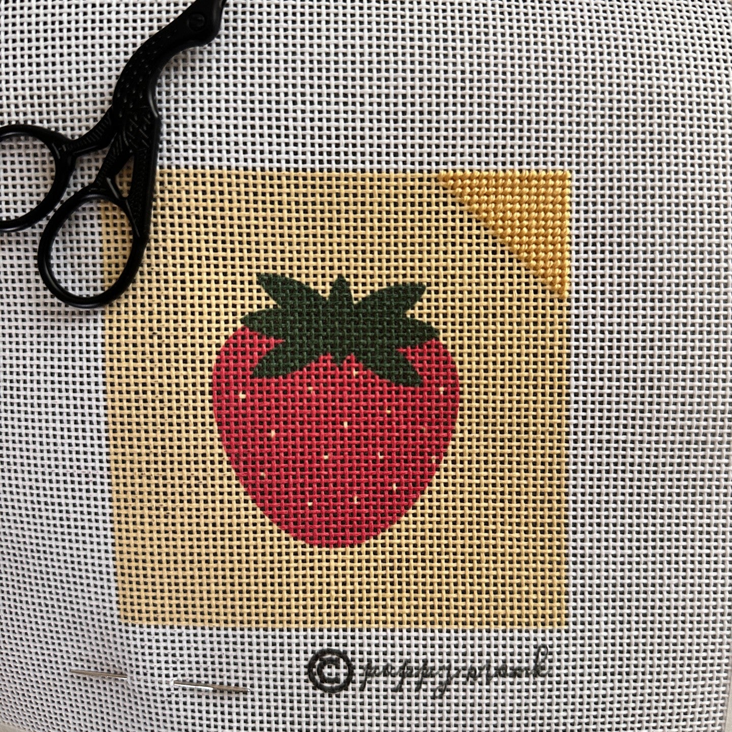 Needlepoint strawberry design partially stitched.