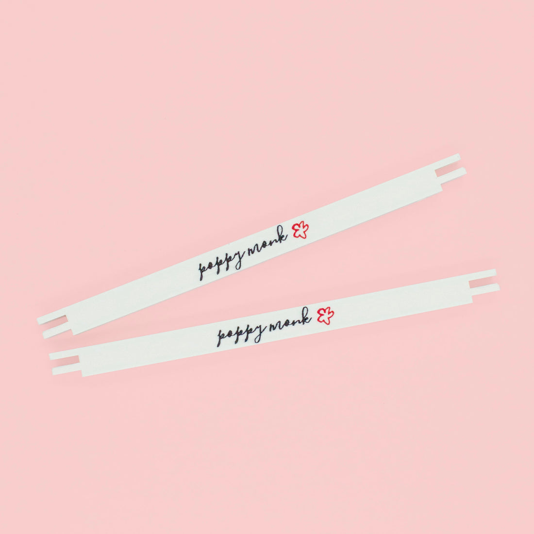 Two white stretcher bars with the Poppy Monk logo printed on them lying on a pink background.