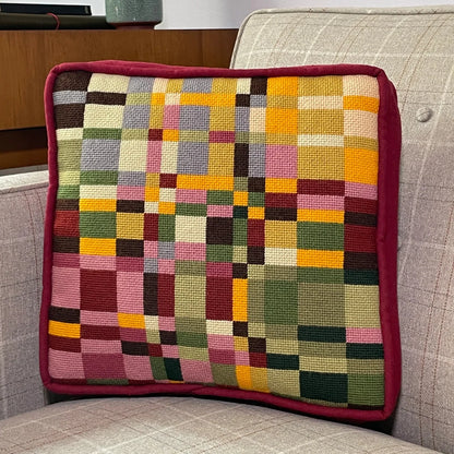 A square needlepoint pillow of geometric design resting on a chair