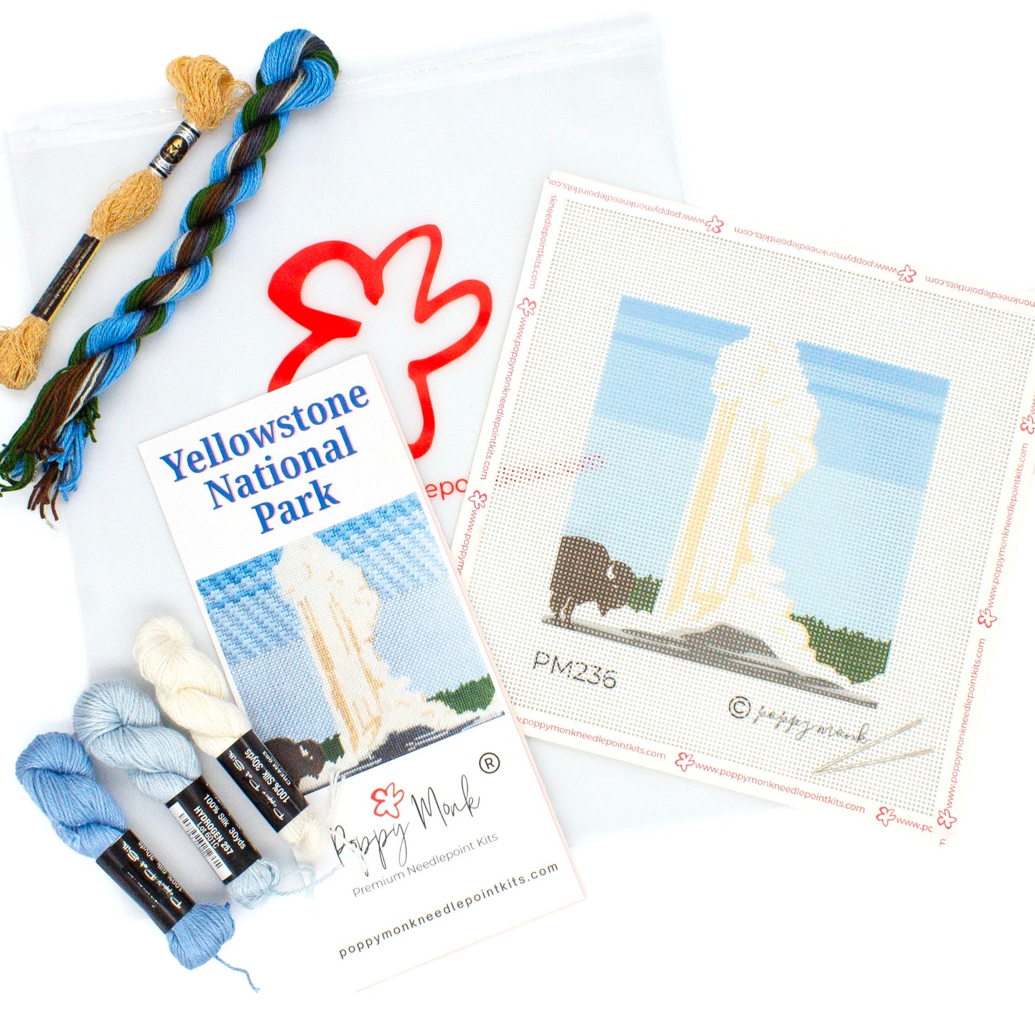 A flat lay of the kit components for the Yellowstone Needlepoint Kit. This includes a canvas with the design printed on it, an instructional brochure, threads, and a clear bag with the Poppy Monk logo on it.