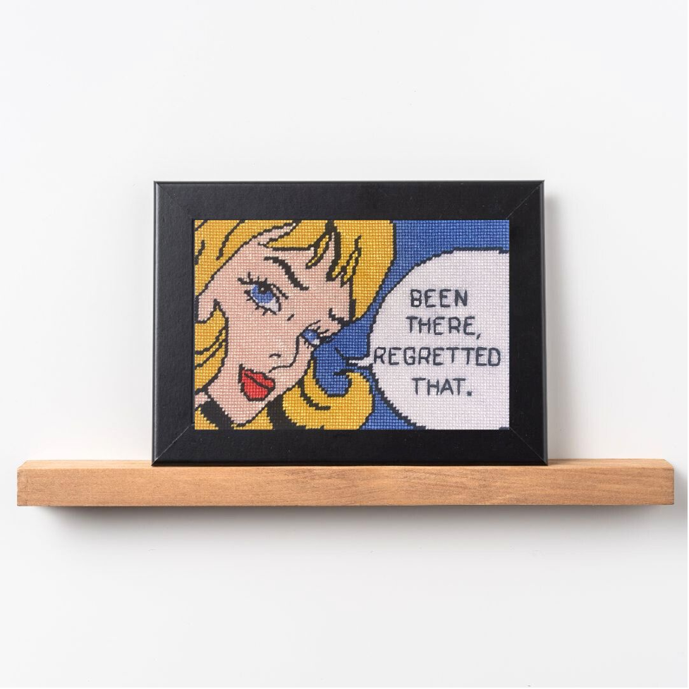 Framed cross-stitch art with a character and text 'Been there, regretted that.' on a white background.