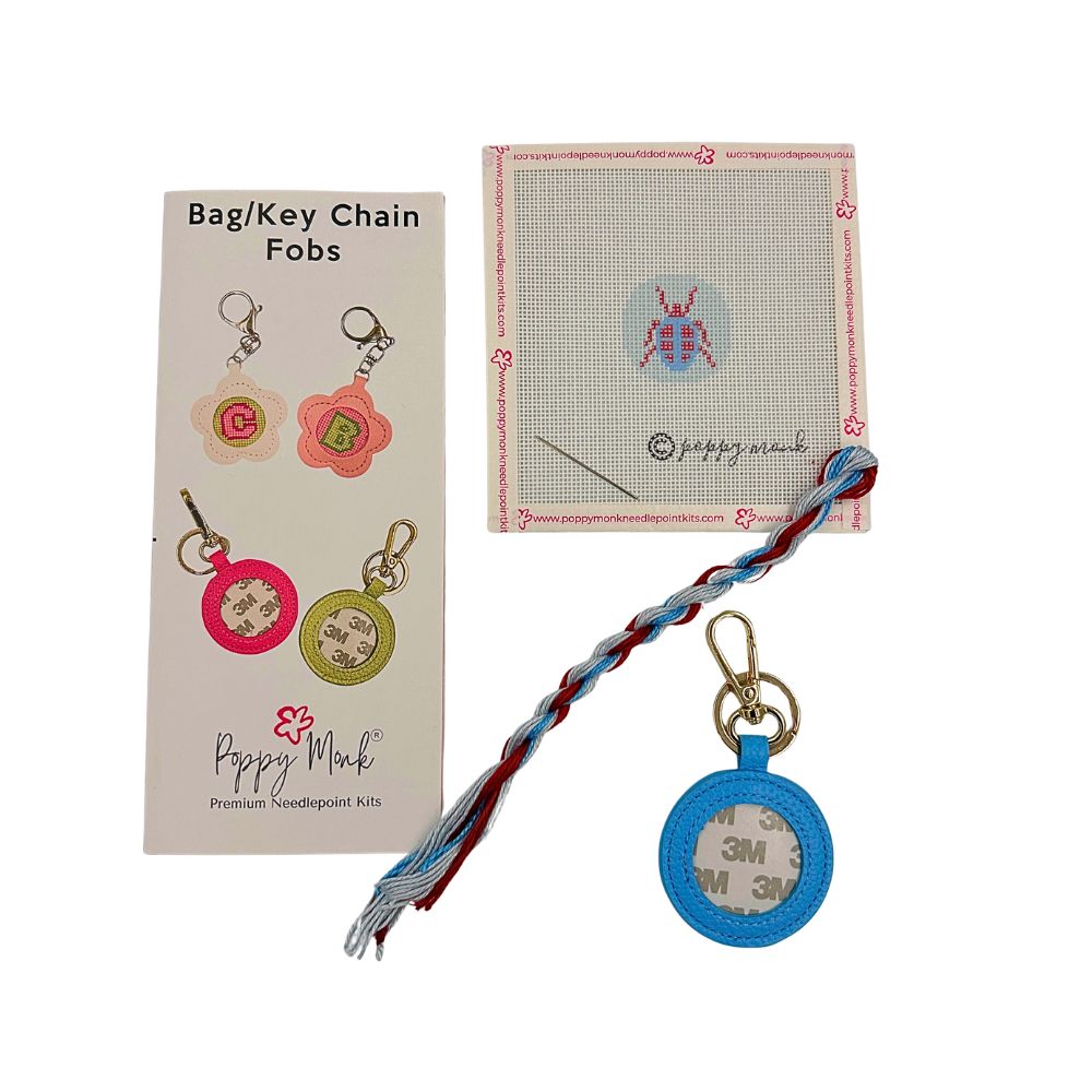 A needlepoint kit with a small blue beetle and a blue fob
