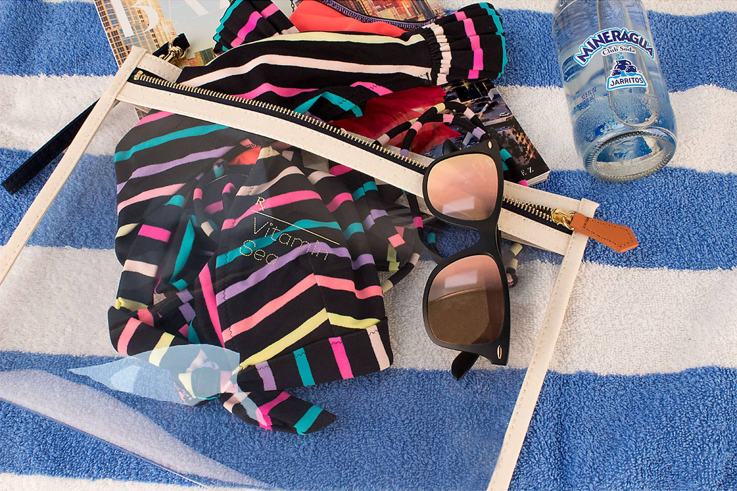 Colorful striped jacket, sunglasses, and a water bottle on a blue and white striped towel