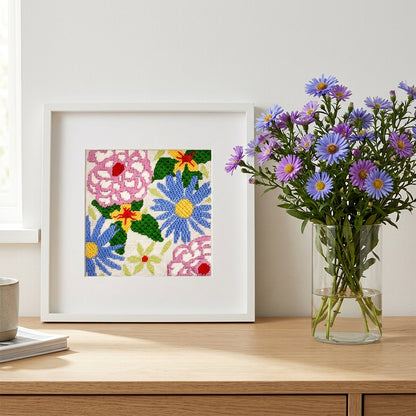 Framed floral needlepoint shown next to a vase of flowers